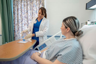 Female Therapist in a female patients room with her. The Therapist is holding an incentive spirometer.
